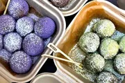 The image shows two trays of colorful dusted truffles, one purple and one green, with a wooden utensil labeled 
