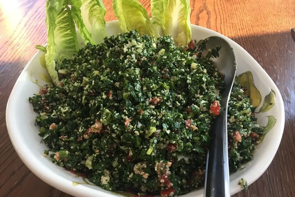 A bowl of tabbouleh a Middle Eastern parsley salad with a serving spoon garnished with romaine lettuce leaves on the side