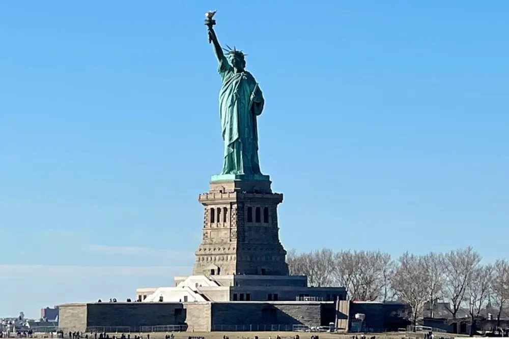 The image shows the Statue of Liberty against a clear blue sky standing on its pedestal on Liberty Island