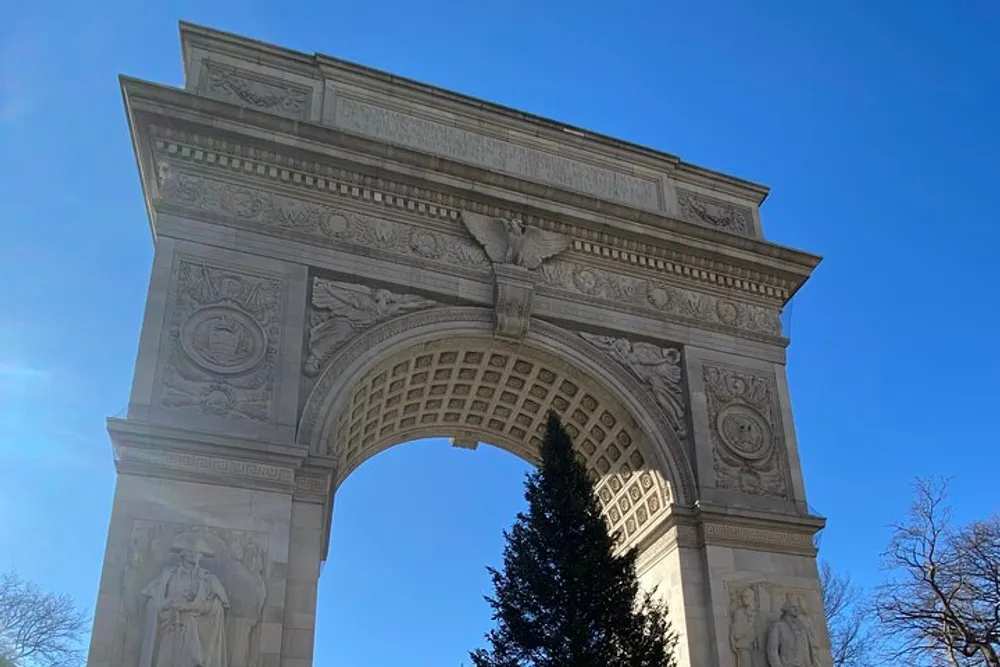 The image shows the Washington Square Arch a marble Roman triumphal arch-style monument located at the northern gateway to Washington Square Park in Manhattan New York City against a clear blue sky