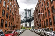 This image features a classic view of the Manhattan Bridge framed by the brick buildings of DUMBO, a neighborhood in Brooklyn, New York.