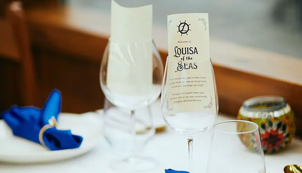 The image shows an elegantly set table with a menu card titled Louisa of the Seas wine glasses a blue napkin and some decorative items suggesting a maritime-themed dining experience