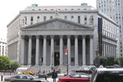 The image shows the imposing facade of a neoclassical courthouse with large columns, pedestrians, and vehicles in the foreground.