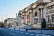 The image showcases the grand and ornate facade of the Metropolitan Museum of Art in New York City on a clear day with the street in the foreground exhibiting minimal traffic and activity.