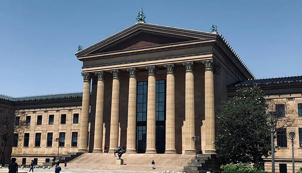 The image shows a large classical building with columns and steps under a clear sky likely a museum or similar institution