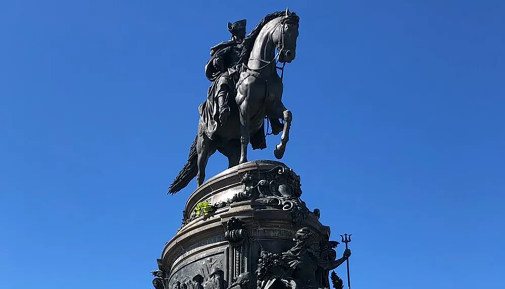 The image shows an equestrian statue of a figure mounted on a rearing horse set against a clear blue sky