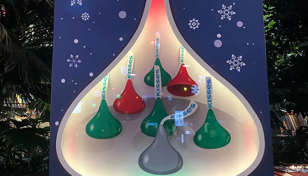 The image features an oversized Christmas-themed Hersheys Kisses candy advertisement displaying an arrangement of large red green and silver-colored Kisses complete with plumes against a backdrop adorned with snowflakes