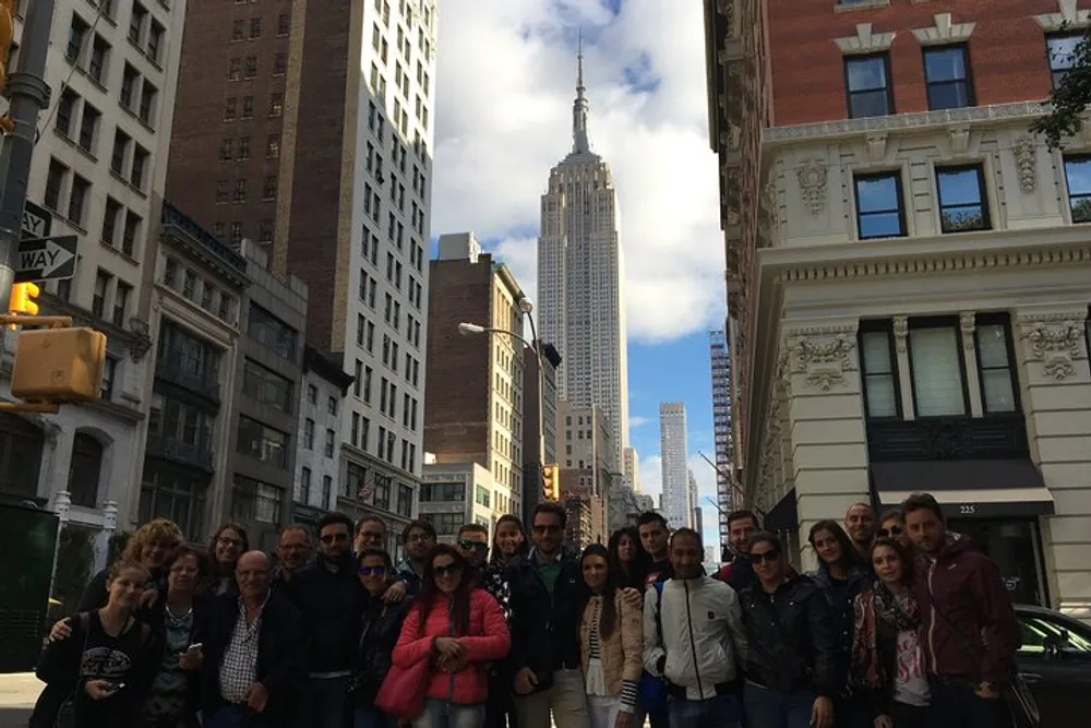 A group of people are posing for a photo on a city street with the Empire State Building in the background
