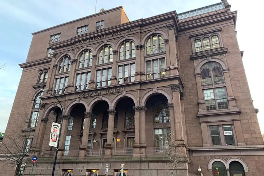The image shows the exterior of the Cooper Union building a historic brownstone facade with arched windows and an inscription stating To Science and Art
