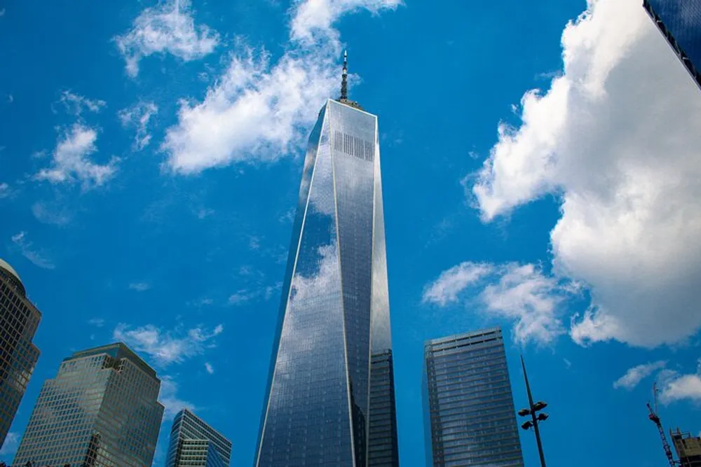 The photo captures a towering skyscraper reaching into a blue sky scattered with clouds flanked by other high-rise buildings