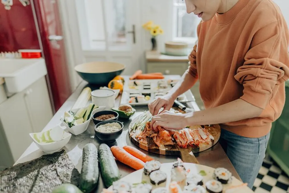 A person is preparing sushi with an array of ingredients and utensils spread across a kitchen counter