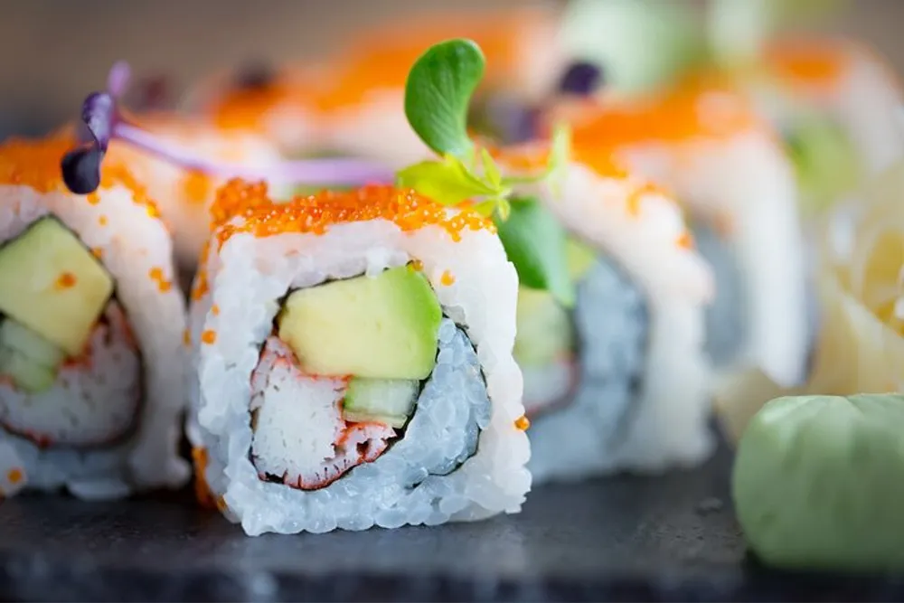 The image features a close-up view of a beautifully presented sushi roll with fish roe and garnish on top
