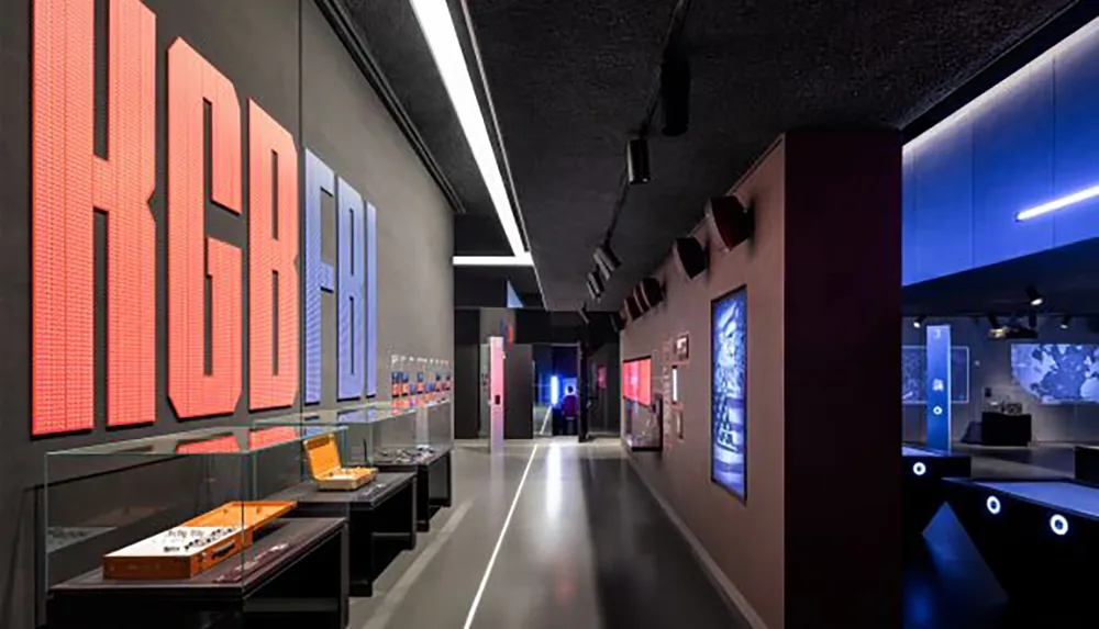 The image depicts a modern and sleek exhibition space illuminated with dynamic lighting and showcasing various displays and interactive elements on dark walls