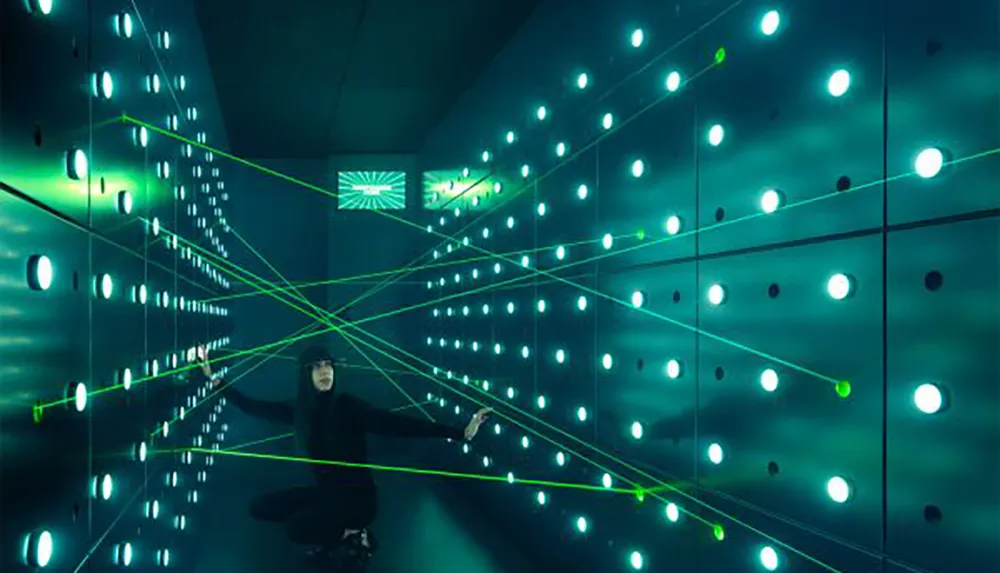 A person interacts with a modern art installation featuring a grid of green illuminated spheres connected by luminous yellow lines in a dark room