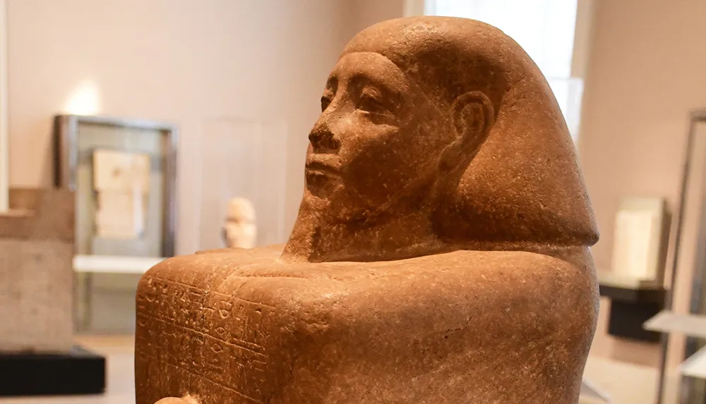 This image features an ancient Egyptian statue with hieroglyphic inscriptions exhibited in a museum gallery with soft lighting