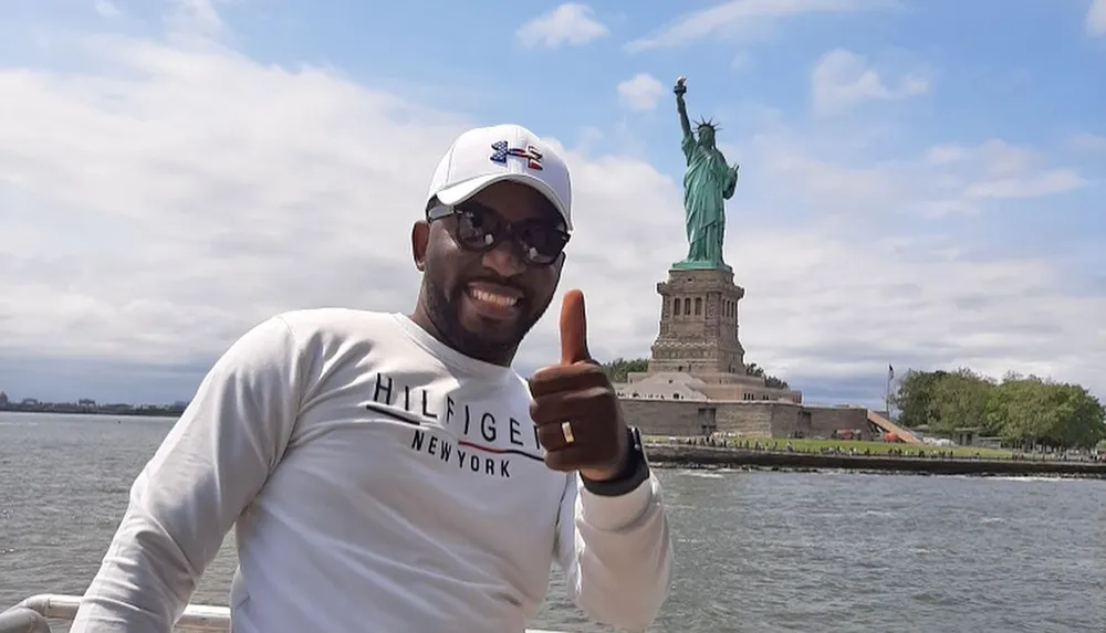 A smiling person is giving a thumbs-up in front of the Statue of Liberty