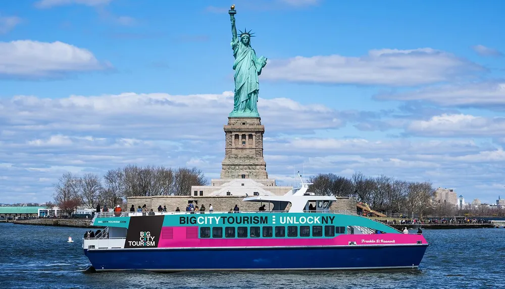 A colorful tourist boat sails near the Statue of Liberty under a blue sky with streaky clouds
