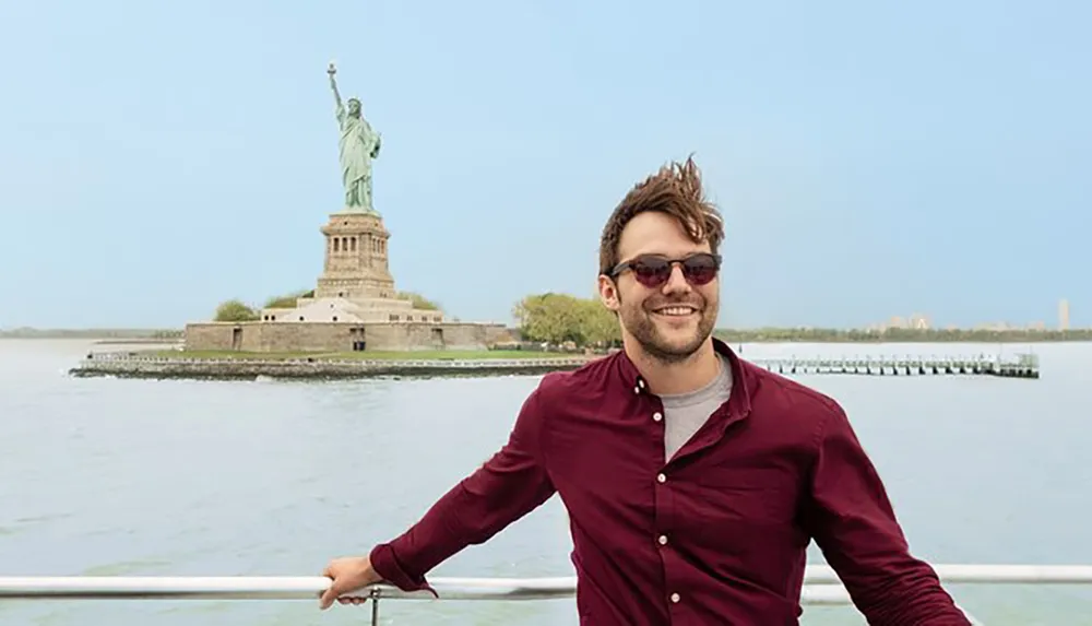A smiling person is posing for a photo in front of the Statue of Liberty