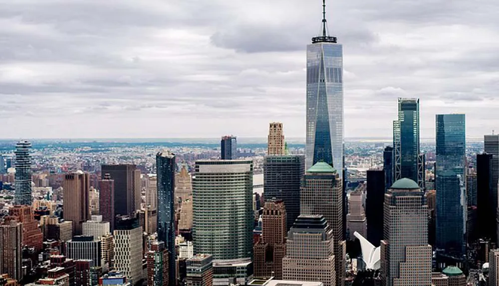 The image is an aerial view of a dense urban skyline dominated by the One World Trade Center amidst numerous skyscrapers likely depicting Lower Manhattan in New York City