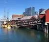 The image features the Boston Tea Party Ships  Museum with a replica of a historical ship moored alongside it set against the backdrop of modern buildings under a clear blue sky