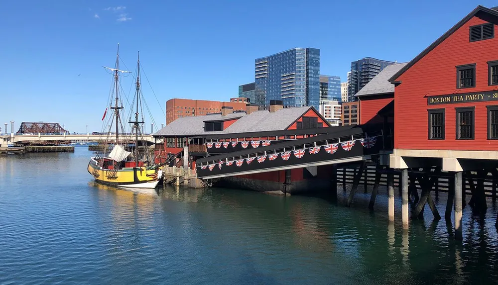 The image features the Boston Tea Party Ships  Museum with a replica of a historical ship moored alongside it set against the backdrop of modern buildings under a clear blue sky