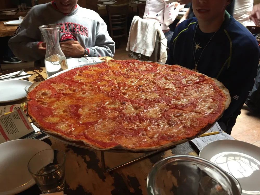 A large pepperoni pizza is on a table surrounded by people ready to enjoy a meal together