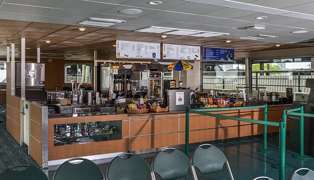 The image shows an empty cafeteria counter with menu displays a selection of snacks and beverages and a roped-off queue area