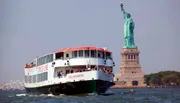 A sightseeing boat filled with tourists is passing by the Statue of Liberty on a clear day.