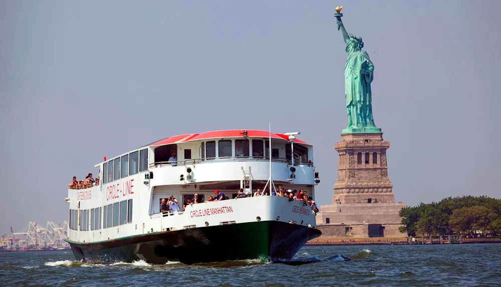 A sightseeing boat filled with tourists is passing by the Statue of Liberty on a clear day