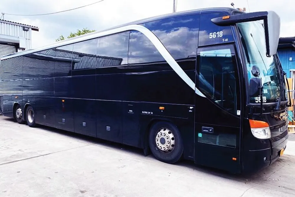 A sleek black tour bus with a modern design is parked at a facility with an overcast sky in the background
