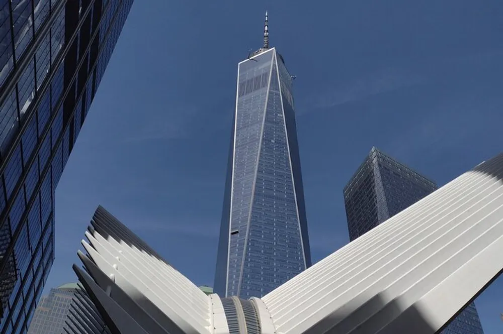 The image features a view of the One World Trade Center skyscraper towering above the Oculus structure at the World Trade Center transportation hub set against a backdrop of a clear blue sky