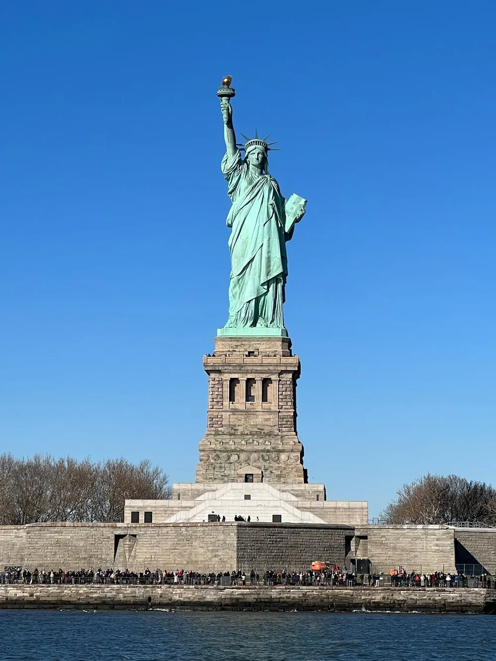 The Statue of Liberty stands tall against a clear blue sky as visitors gather around its pedestal on Liberty Island