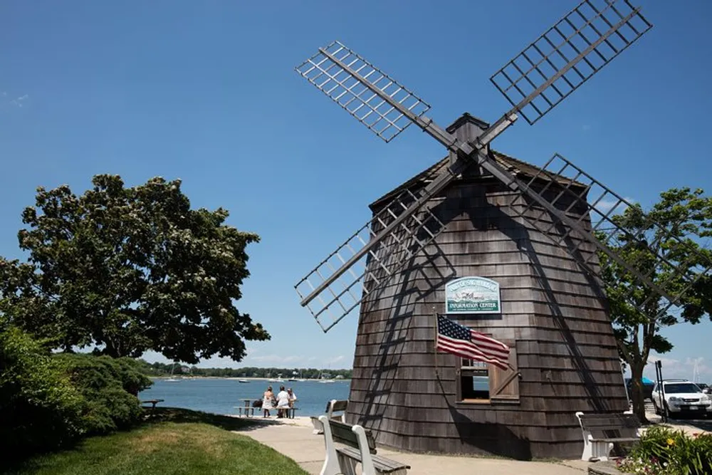 The image features a traditional windmill by the water with people walking nearby set against a clear blue sky
