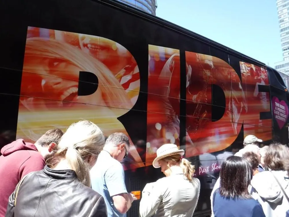 A group of people is lined up beside a bus with a large bold RIDE advertisement on its side