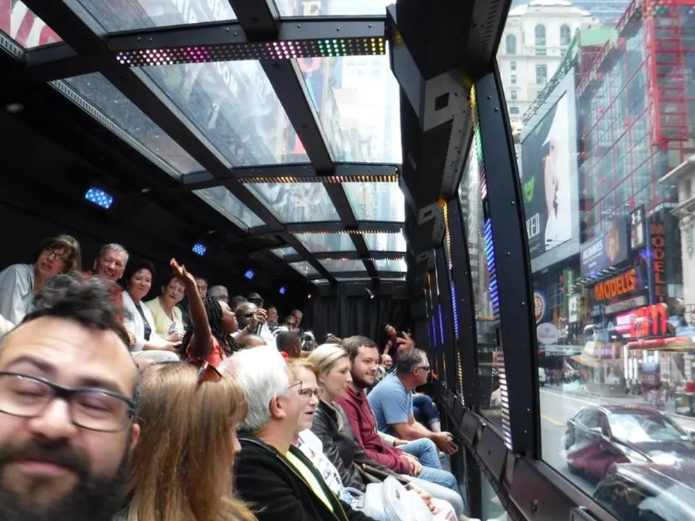 A group of tourists is enjoying a sightseeing tour on a bus with large windows offering views of a vibrant urban streetscape