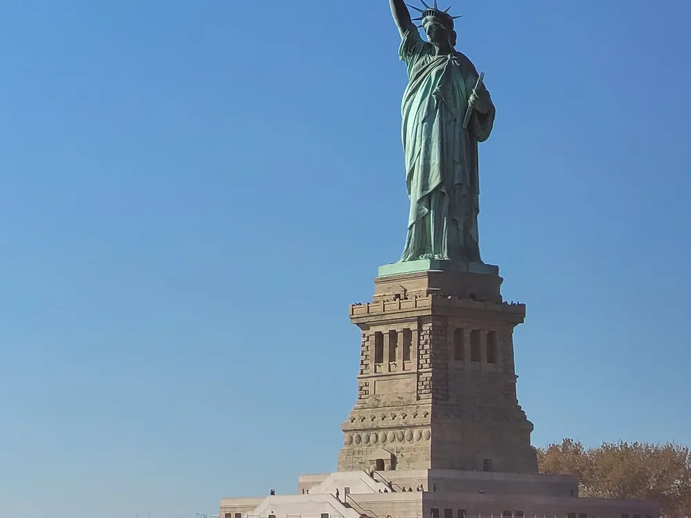 The image shows the Statue of Liberty against a clear blue sky standing tall on its pedestal