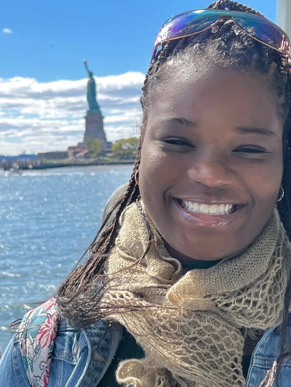 A smiling person poses for a photo with the Statue of Liberty in the background