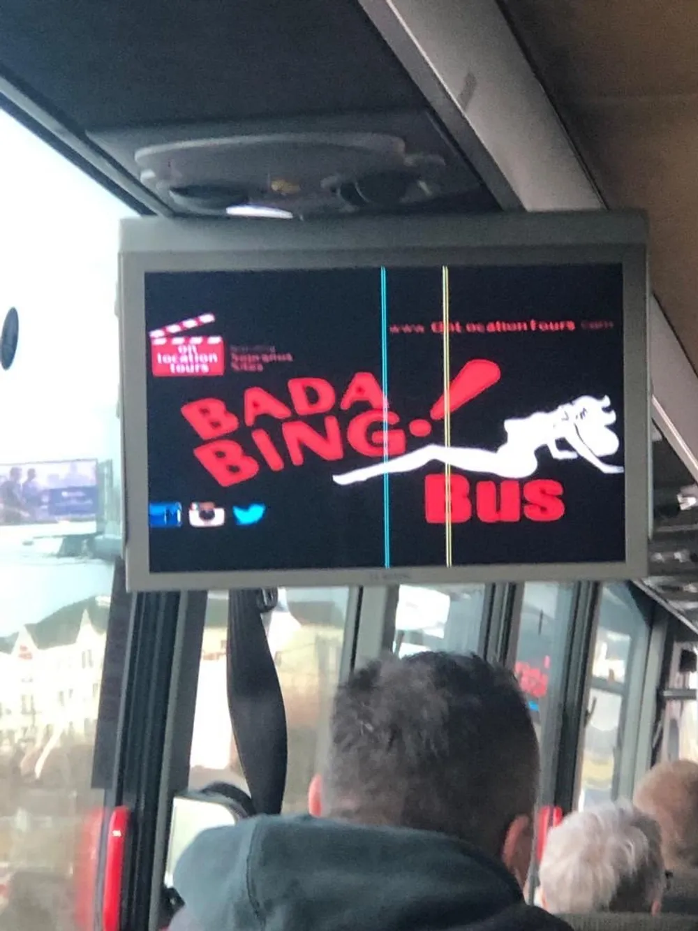 The image shows a digital display inside a bus with the words BADA BING BUS in red letters an outline of a bull and blurry background that indicates it might be taken from a moving vehicle or in a crowded setting