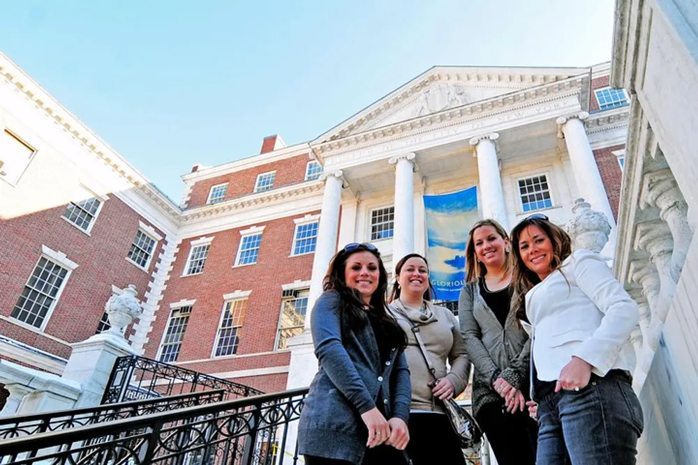 Four smiling individuals pose in front of a building with classical architecture featuring a pillared entrance and a blue banner
