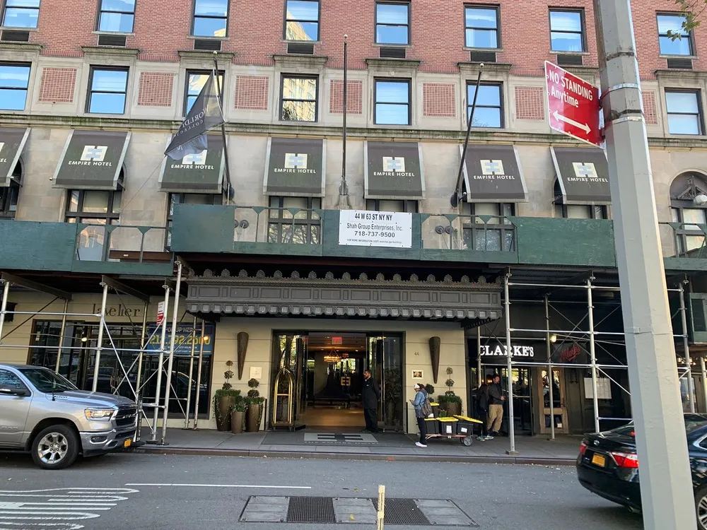 The image displays the street-level view of the Empire Hotel with its entrance awning and signage on a sunny day with pedestrians and vehicles visible