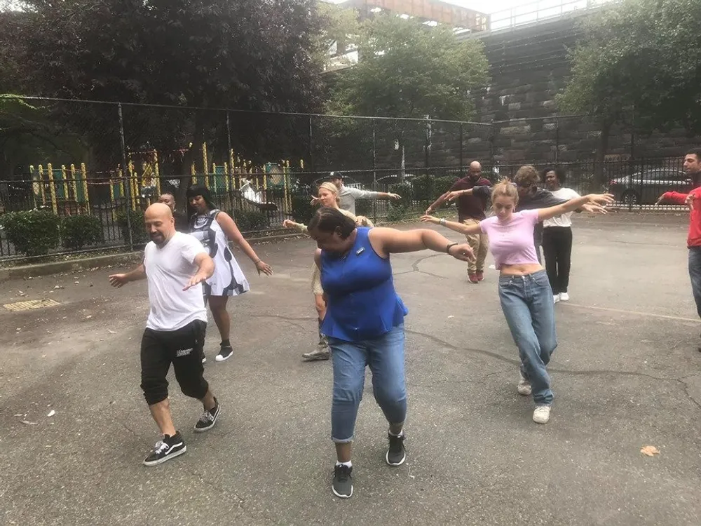 A diverse group of people appears to be joyfully participating in an outdoor dance class or activity in an urban park setting