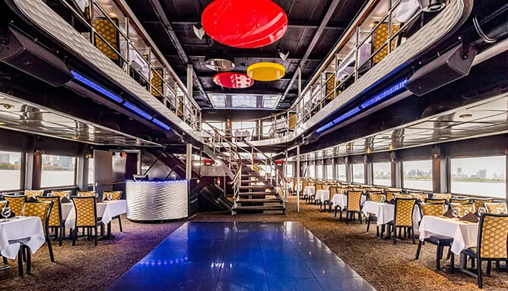 The image shows a modern two-tiered dining area with colorful overhead lighting a dance floor and a view of the water through large windows