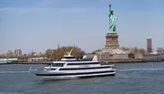 A City Cruises boat sails near the Statue of Liberty under a clear blue sky.