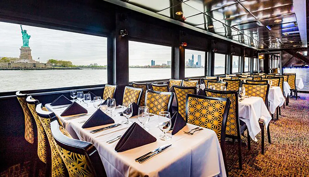 An elegant dining area inside a boat offers a stunning view of the Statue of Liberty through large windows