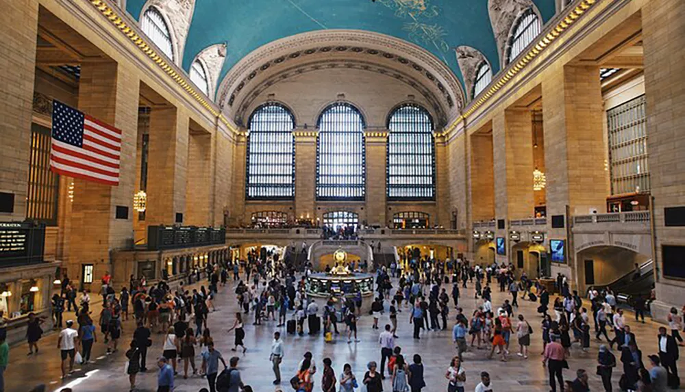 The image shows a busy grand hall with high ceilings large windows and an American flag indicative of a major transport hub
