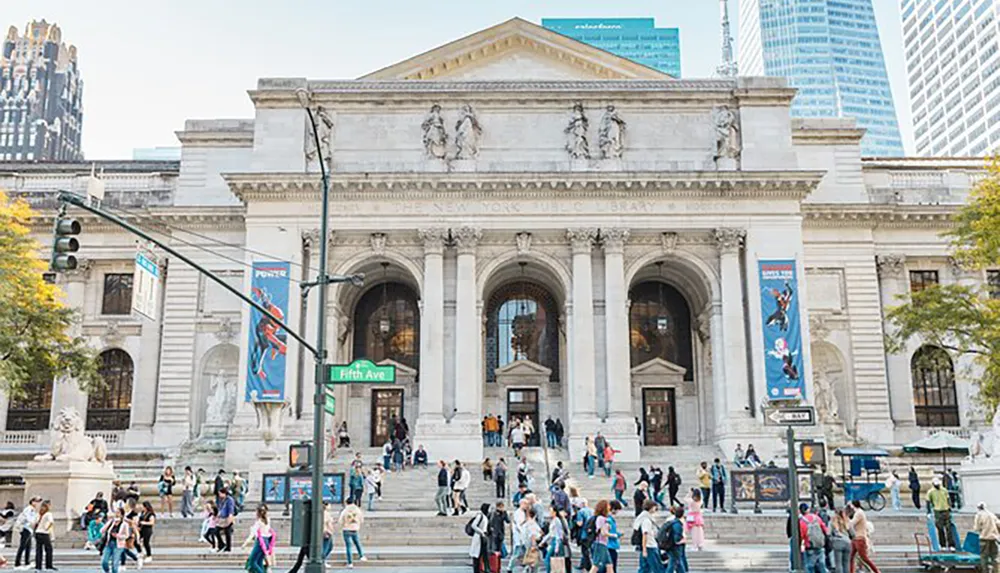 This image shows a bustling scene in front of the iconic New York Public Library with pedestrians and banners against a backdrop of skyscrapers