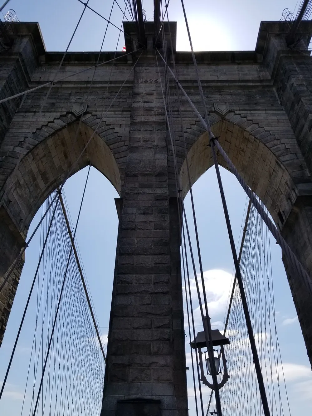 The image shows an upward view of a towering stone bridge pillar with numerous suspension cables possibly part of an iconic suspension bridge
