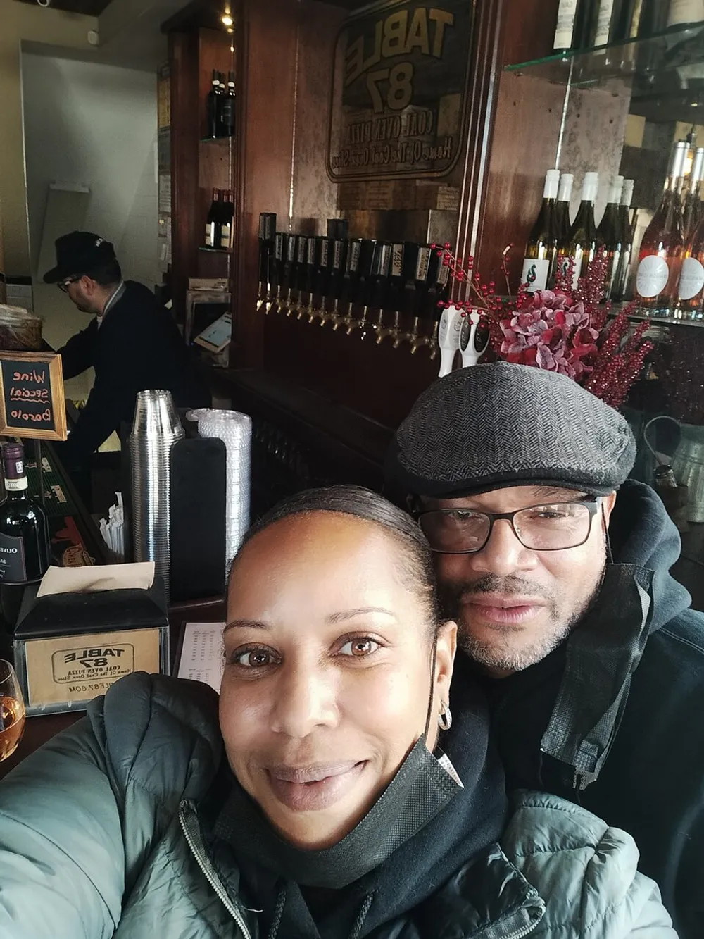 A man and a woman are taking a selfie together with a cozy bar setting in the background