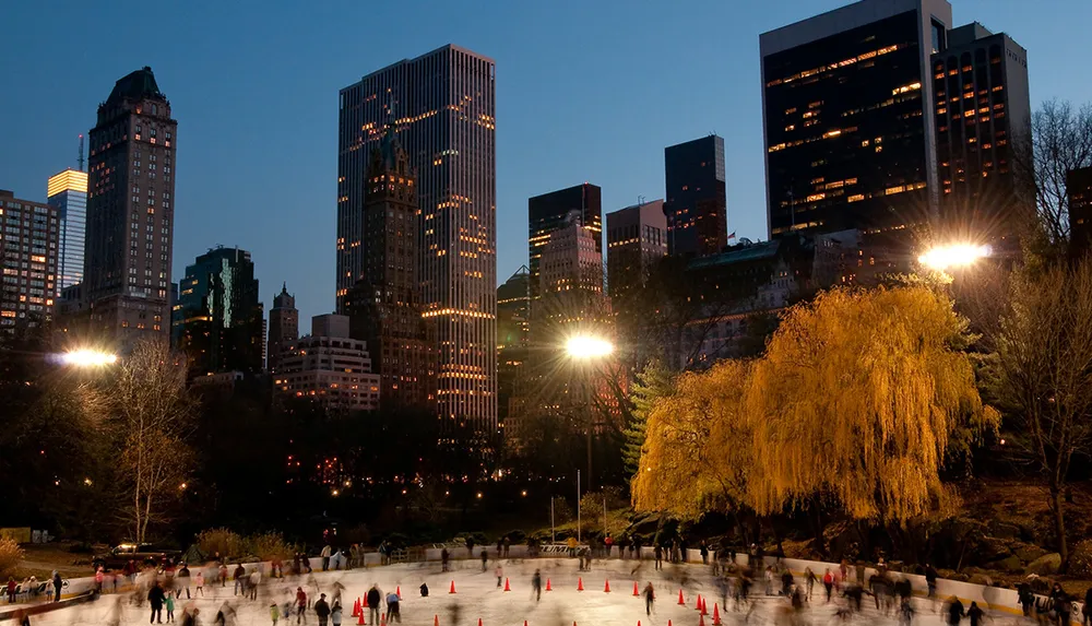 Skaters enjoy an evening on an outdoor ice rink in a city park surrounded by towering skyscrapers and glowing city lights at dusk