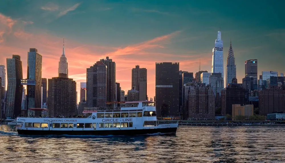 A sightseeing cruise boat sails along the water in front of a striking New York City skyline at sunset